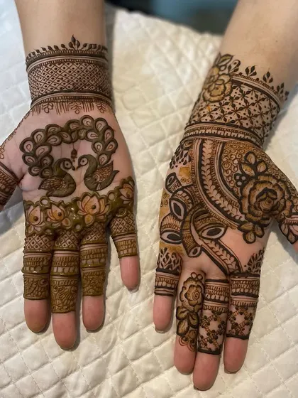 A unique Karwachauth design with different motifs on each hand. One features two peacocks, while the other has a more abstract, face-like pattern.