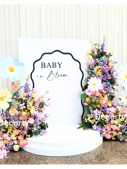A 'Baby in Bloom' backdrop with a different design, featuring a wavy border and colorful floral arrangements with large daisy props.