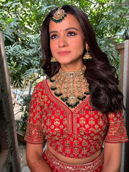 A stunning portrait against a natural backdrop. The red lehenga and green jewelry are perfectly complemented by the soft glam makeup.