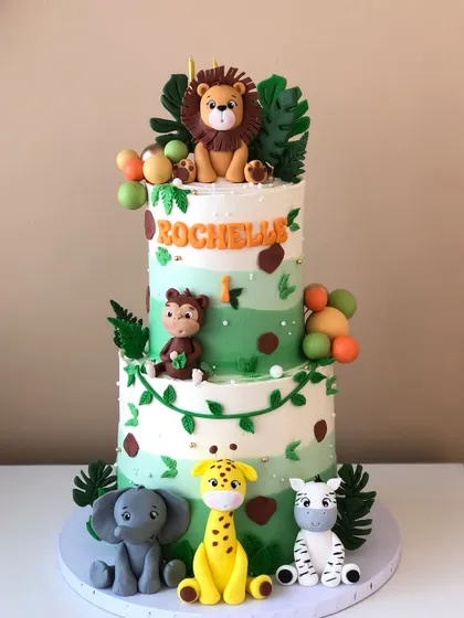A full view of the two-tiered safari cake, with a lion on top and a monkey swinging from a vine.