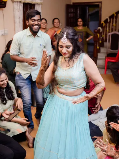 Fun and candid moments from a mehendi ceremony. The bride's makeup is fresh and playful, with a winged liner and glowing skin, perfect for celebrating with her loved ones. The hairstyle is a soft half-updo with pretty accessories.