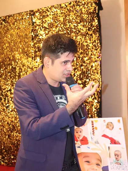 Addressing the audience in front of a glittering gold backdrop, perfect for a glamorous birthday party.