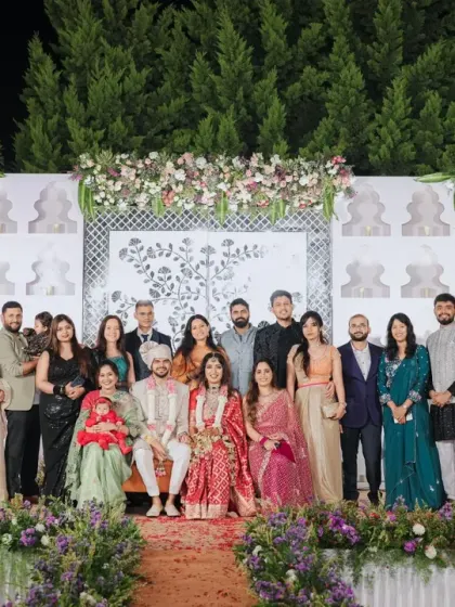 The couple and their families pose for a group photo on the elegant, Sheesh Mahal-inspired reception stage.