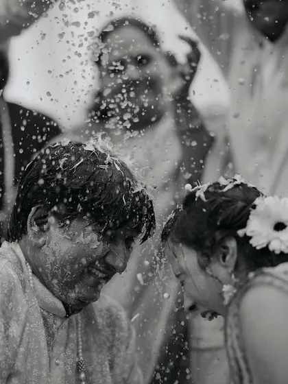 A black and white photo capturing the fun and chaos of a Haldi ceremony, with the couple laughing as they are covered in turmeric and water.