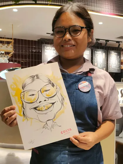 A Costa Coffee staff member with her very own caricature, a fun moment during the event.