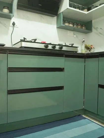A beautiful L-shaped kitchen with glossy green cabinets and a white marble-effect backsplash. The design includes open shelving and under-cabinet lighting, creating a fresh and modern look.