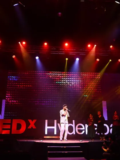 I perform on the TEDx Hyderabad stage, with my live image on the screens and red lights across the room.