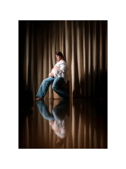 An artistic and modern studio portrait featuring a mom-to-be in casual jeans and a white shirt. The reflection on the floor adds a layer of depth and contemplation to this intimate maternity photo.