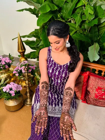 A beautiful bride in a purple outfit, admiring her modern geometric mehndi design.