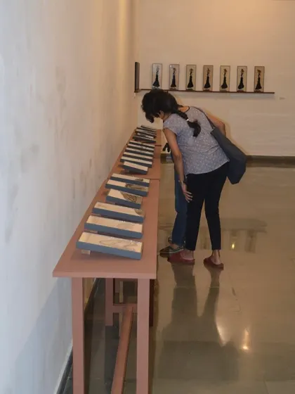 A visitor looking closely at the details in a series of reverse paintings by Shakuntala Kulkarni.