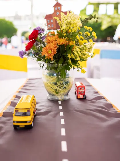 A creative table runner designed to look like a road for a "Wheels on the Bus" party. Miniature buses and a floral centerpiece complete this unique and thematic table decoration.