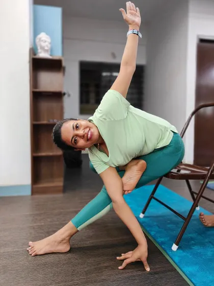 A smiling student enjoys a modified triangle pose using a chair for support and balance.