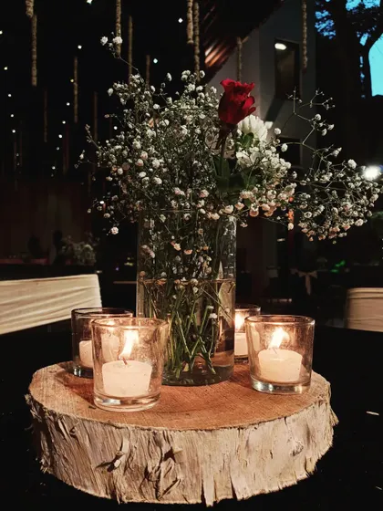 A rustic yet elegant centerpiece featuring a wooden log base, candles, and a simple arrangement of baby's breath and a single red rose.