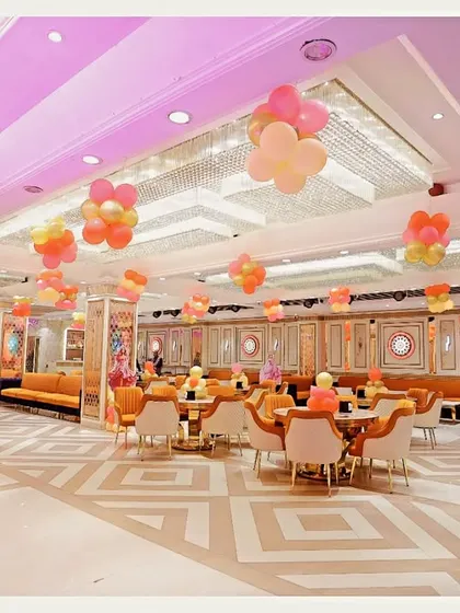 The elegant interior of the banquet hall, decorated with balloons for the birthday party. The pink and orange color scheme creates a warm and festive atmosphere.