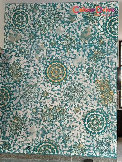 This accent wall showcases a vibrant Calcecruda texture combined with a bold mandala stencil design. The teal, white, and gold color combination creates a striking and artistic statement piece for any room.