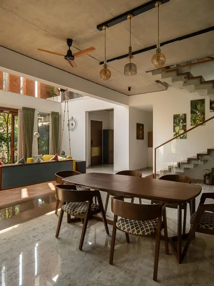 The dining area flows seamlessly from the living space, unified by an exposed concrete ceiling and views of the garden. The use of marble flooring here differentiates the zone while maintaining an open feel.