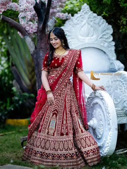 The grand red velvet lehenga is shown here in a beautiful garden setting, proving its versatility for both indoor and outdoor shoots.