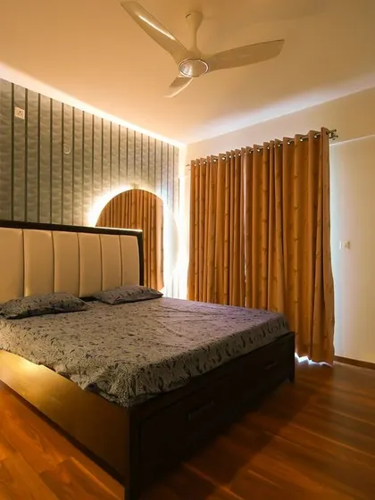 This bedroom design focuses on clean, minimal lines, featuring a textured accent wall with an integrated backlit mirror, warm wood floors, and simple, elegant furnishings.