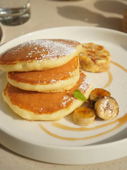 A stack of our light and fluffy pancakes, dusted with powdered sugar and served with caramelized bananas and a drizzle of syrup. A sweet treat for any time of day.