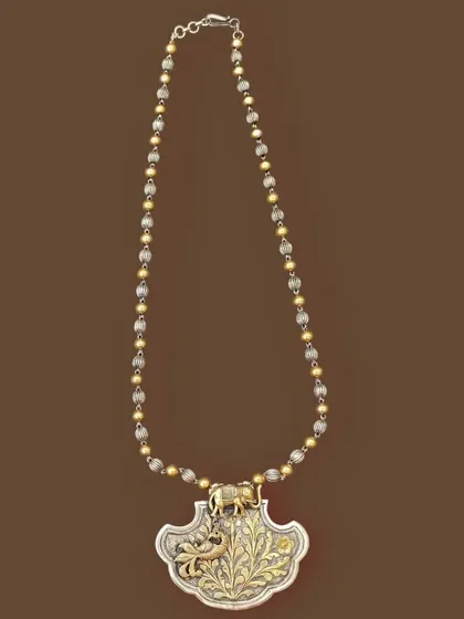 An example of my unique dual-tone work. This necklace features a silver pendant with a gold-plated floral design and an elephant motif, strung on a chain of alternating silver and gold beads.
