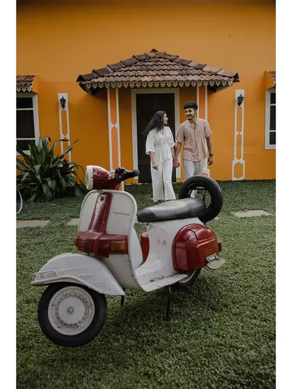 A full shot of a couple with a vintage scooter in front of a colorful house.