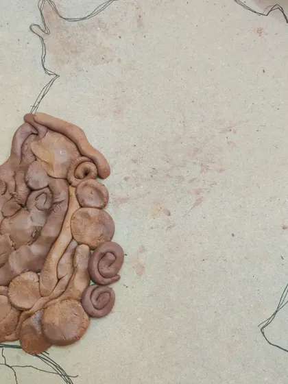 The beginning of a clay silhouette project. A child starts to fill in the outlined profile with small, shaped pieces of clay, focusing on one section at a time in this mindful art activity.