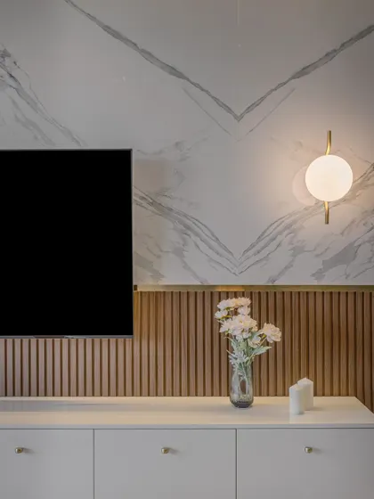 We love to mix materials for a rich, textural effect. This TV wall combines a book-matched marble pattern with fluted wood paneling below. A simple white console and a modern globe wall sconce complete this clean yet sophisticated composition.