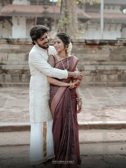 A classic portrait of a South Indian couple standing together in front of a temple, showcasing their elegant wedding attire.