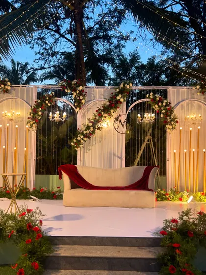 A beautiful stage setup for a wedding reception, with a classic white sofa, elegant floral arches, and warm candle-like lighting.