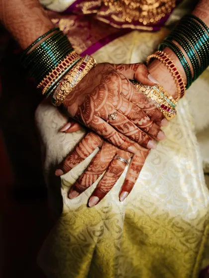 A close-up shot of the bride's hands, adorned with intricate henna and traditional green bangles.