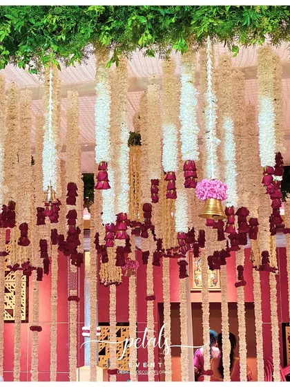 A dense curtain of tuberose, chrysanthemum, and rose streamers creates a fragrant and visually stunning backdrop for the ceremony. The hanging temple bells add a musical element to the decor.