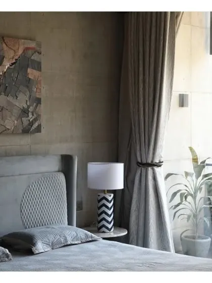 This tranquil bedroom in Swatantra Residence features a symphony of materials and textures. The concrete ceiling and walls provide an industrial backdrop for the soft, elegant furnishings and abstract artwork.
