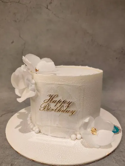 A minimalist and aesthetic white birthday cake. The simple textured finish and delicate sugar flowers create a look of pure elegance.