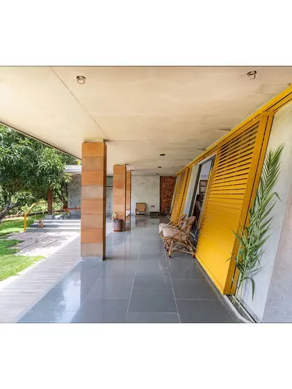 The long, shaded verandah at "Aamra," with its distinctive yellow angled shutters. This space acts as a buffer zone, protecting the interiors from the sun while providing a comfortable place to enjoy the view of the mango orchard.