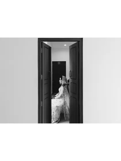 A creative black and white shot of a bride seen through a doorway. This framing adds a sense of mystery and artistry to the bridal portrait.