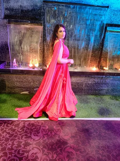 A client looking stunning in a custom red draped gown for an evening event. The design features a flowing, cape-like sleeve for a dramatic and elegant effect.
