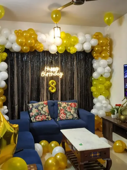 A yellow and white balloon arch with a neon sign for an 8th birthday, elegantly arranged around a living room sofa.