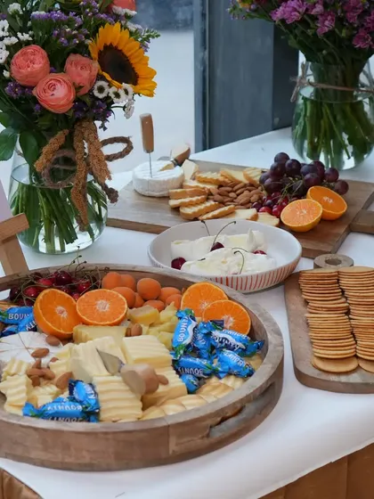 A rustic and inviting cheese board setup for an event at Varnya. The platter features a mix of cheeses, crackers, almonds, and fresh fruits, complemented by beautiful sunflower bouquets.