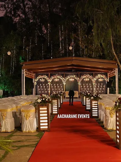 A view from the aisle of the outdoor reception setup. The red carpet leads the eye to the beautifully lit stage, while hanging lights in the surrounding trees add to the magical, open-air ambiance.