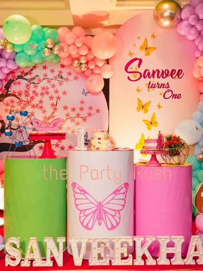 Sanveekha's first birthday combined butterflies and fairies for a whimsical celebration. The setup includes a cherry blossom backdrop, fairy wing cutouts, and a pastel balloon arch, creating a dreamy and colorful scene.