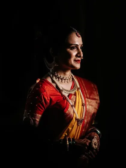 A dramatic bridal portrait using chiaroscuro lighting. The bride emerges from the darkness, her traditional yellow and red saree glowing, creating a powerful and artistic image.