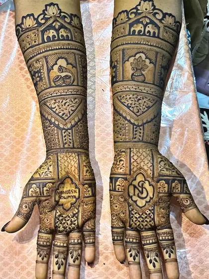 This custom bridal design features the couple's initials and wedding name, surrounded by traditional motifs. The top of the arms is adorned with domes and elephants, symbolizing a grand celebration.