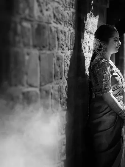 A moody and atmospheric black and white portrait. The bride stands against a stone wall with a hint of smoke, creating a cinematic and timeless feel.