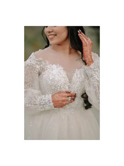 A close-up on the bride's stunning white gown. This shot highlights the intricate beadwork on the sleeves and her beautiful henna, details that make her look unique.