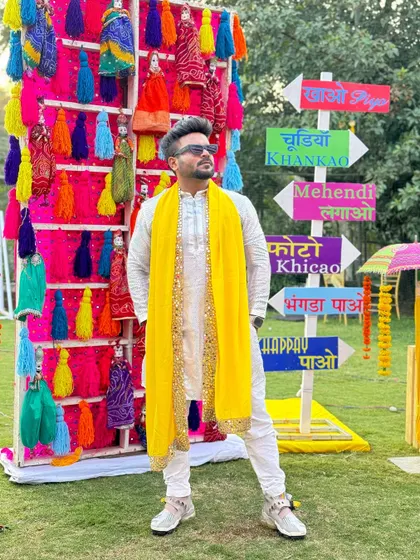 Posing against a quirky, colorful photo booth at a Mehendi carnival. The decor sets the tone, and I bring the vibe.