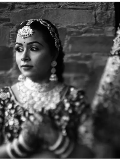 A soft-focus black and white portrait of the bride, her expression serene and thoughtful, highlighting her traditional maang tikka.