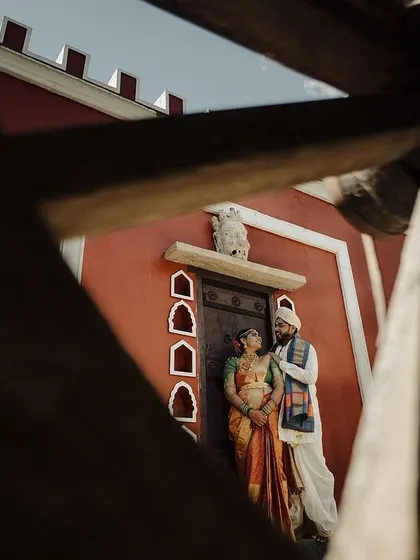 A creatively framed shot of the couple against a striking red wall. Using architectural elements to frame the portrait adds an artistic and dramatic touch to their wedding album.