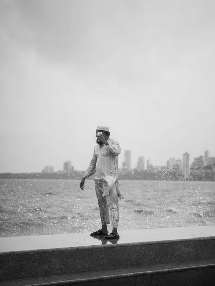 A black and white photo series capturing the spirit of Mumbai's monsoon at Marine Drive. People are seen enjoying the high tide, getting drenched by waves, and finding joy in the downpour.