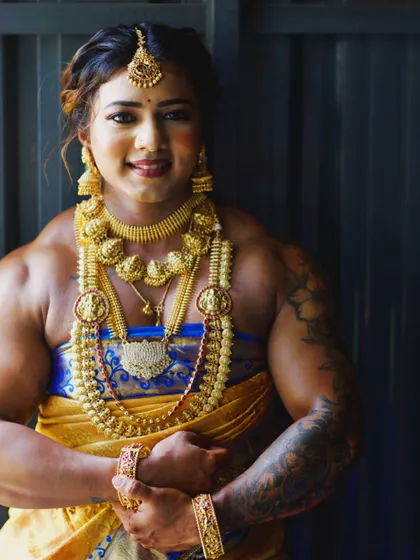 A smiling pose in a blue and gold saree. The heavy temple jewelry complements the powerful physique, showcasing a unique blend of grace and strength.