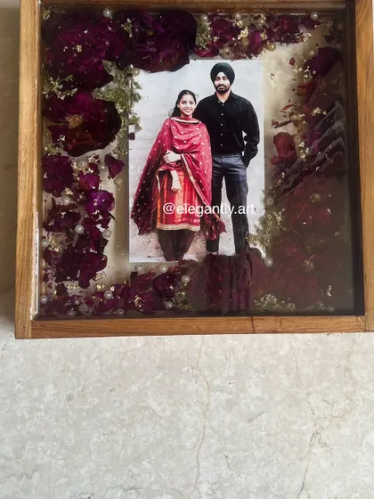 A simple and elegant teakwood frame preserving red rose petals from a wedding. The minimalist design puts the focus on the couple's photo and the rich color of the roses.